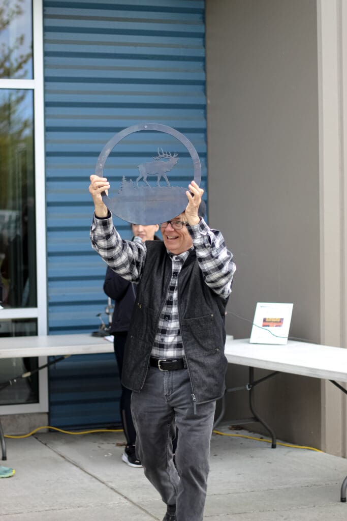 Man holds round welded sign with wildlife carved in
